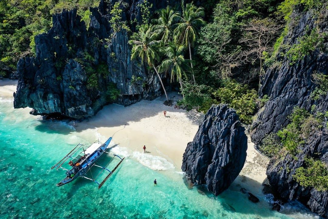 Limestone cliffs rising above clear water and a bangka boat in El Nido, Palawan, Philippines