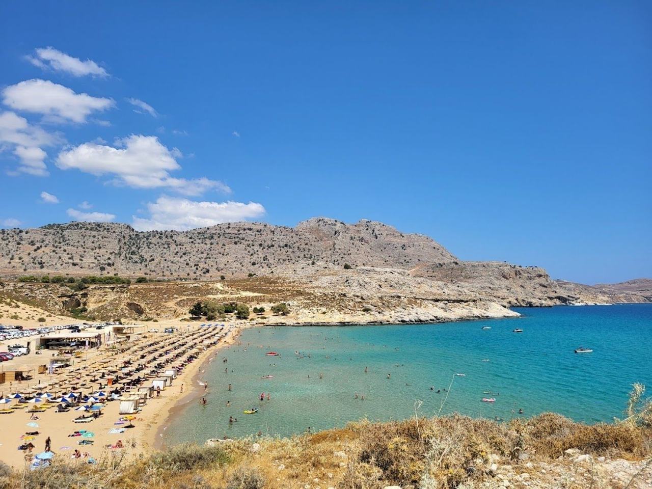View over the golden sand and clear shallow bay of Agathi beach with the ruined Feraklos castle on the hill behind on the east coast of Rhodes