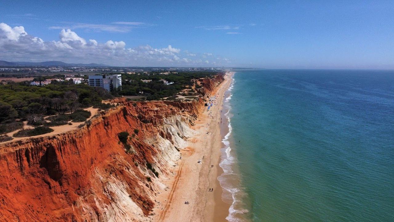 Long golden sand backed by red cliffs and calm water at Falesia beach in the Algarve