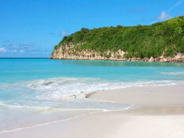 Soft white sand and calm turquoise water under blue sky on a clear day at Dickenson Bay in Antigua