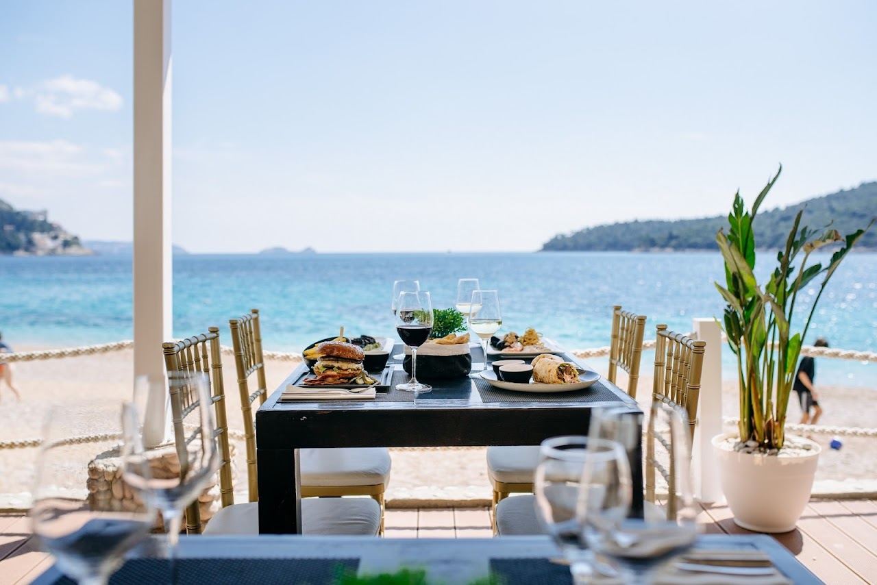 Lounge beds and umbrellas of the Banje Beach club on the pebbles with Dubrovnik Old Town walls behind