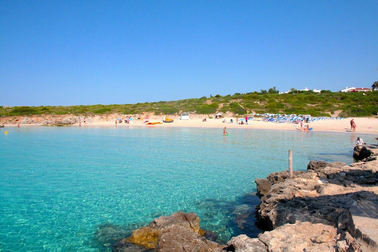 Calm shallow golden sand cove with clear water at Binibeca beach in Menorca