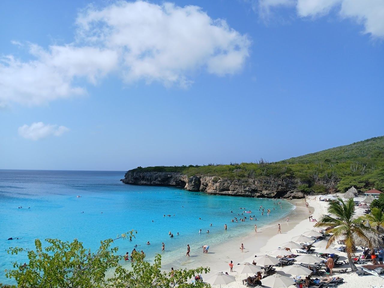 Soft white sand, turquoise water and limestone cliffs on a calm sunny day at a cove on Curacao