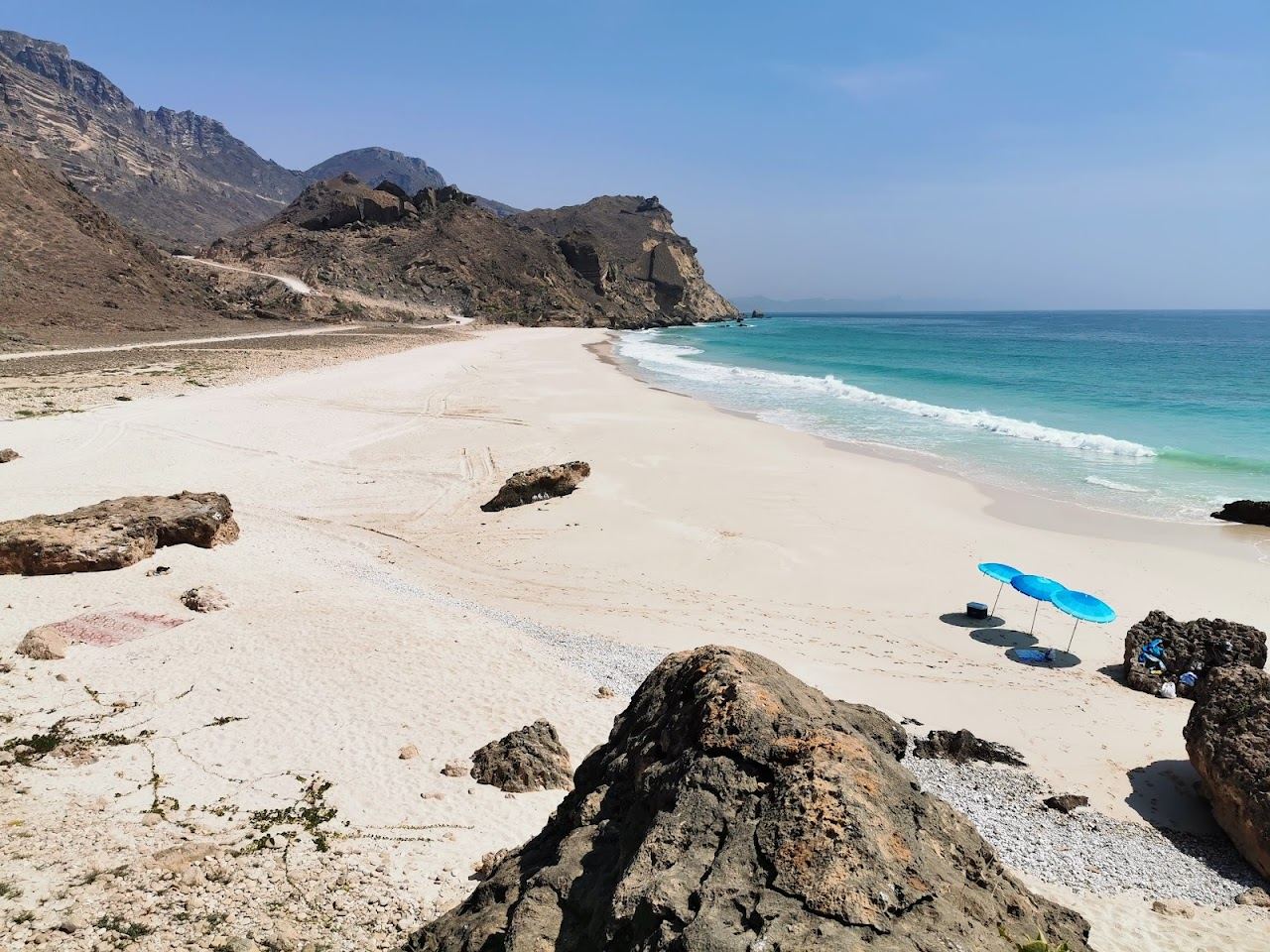 Pale sand and clear turquoise water in a remote cove below cliffs at Fazayah beach west of Salalah