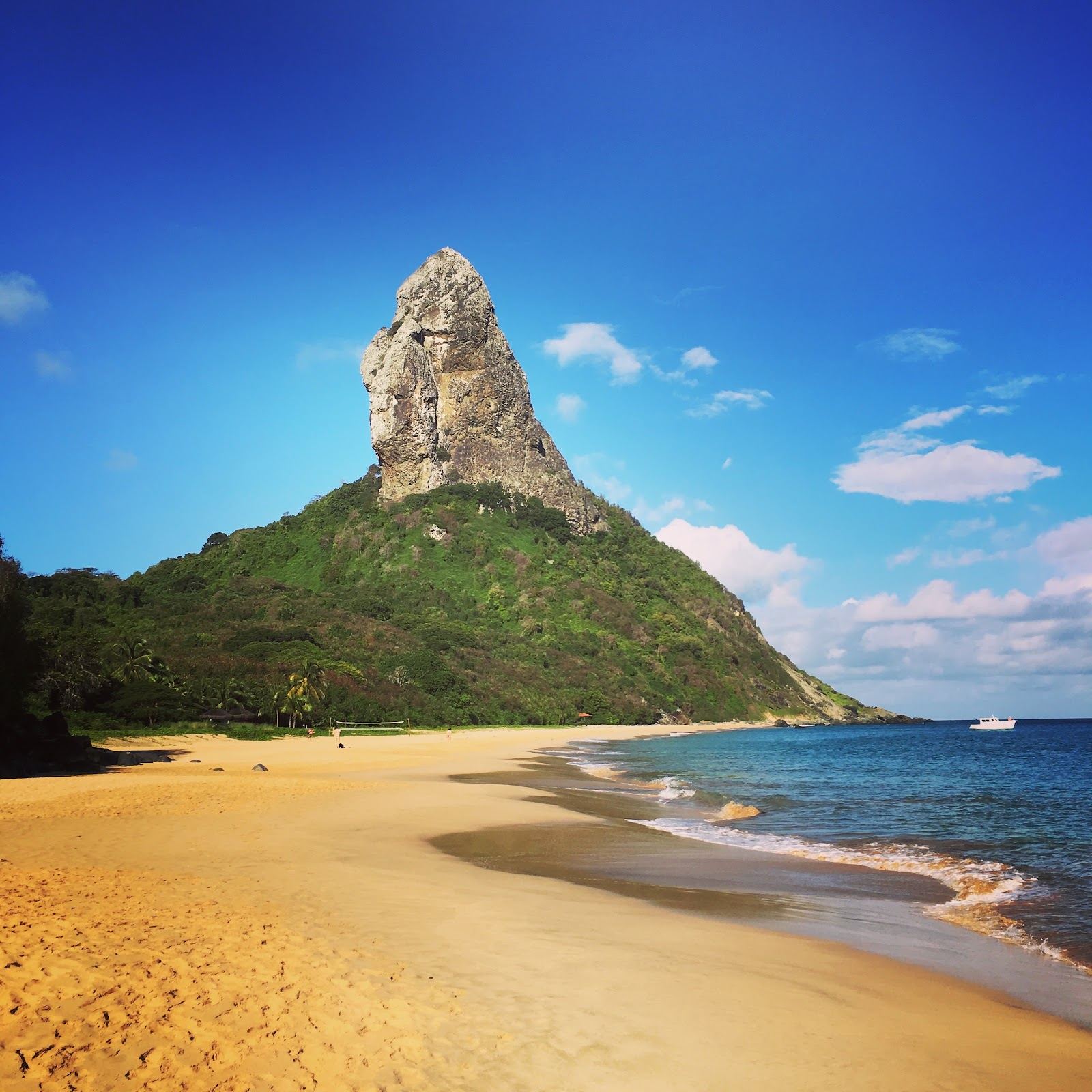 Golden sand and emerald water at Praia da Conceicao below the peak of Morro do Pico in Fernando de Noronha