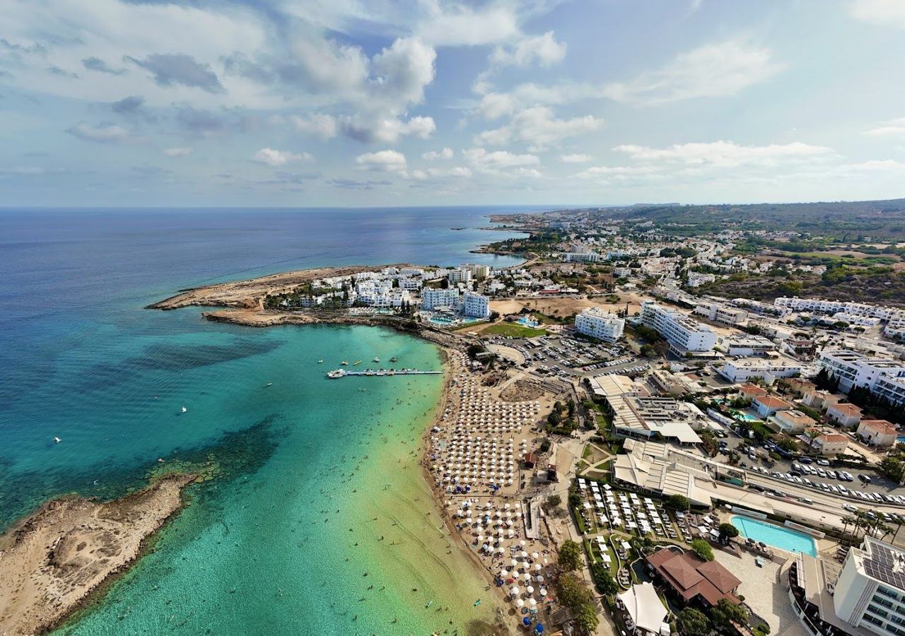 White sand and clear shallow turquoise water with a small islet offshore at Fig Tree Bay in Protaras Cyprus