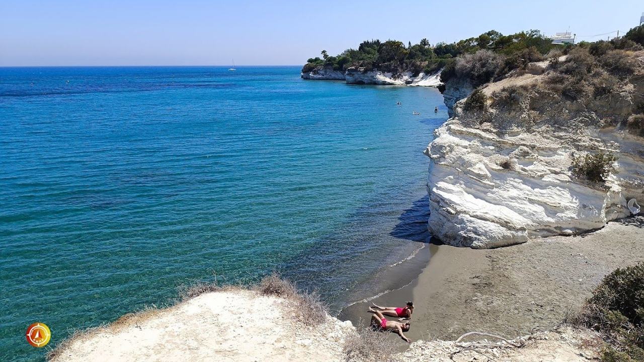 Small cove of dark sand below bright white chalk cliffs with clear water at Governor's Beach in Cyprus