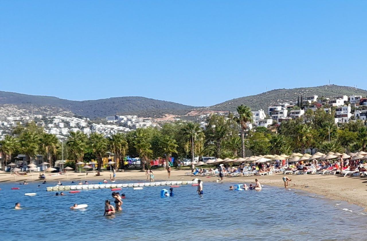 Gumbet Beach near Bodrum with a curve of sand and shingle, moored boats and a waterfront of bars and beach clubs in Turkey