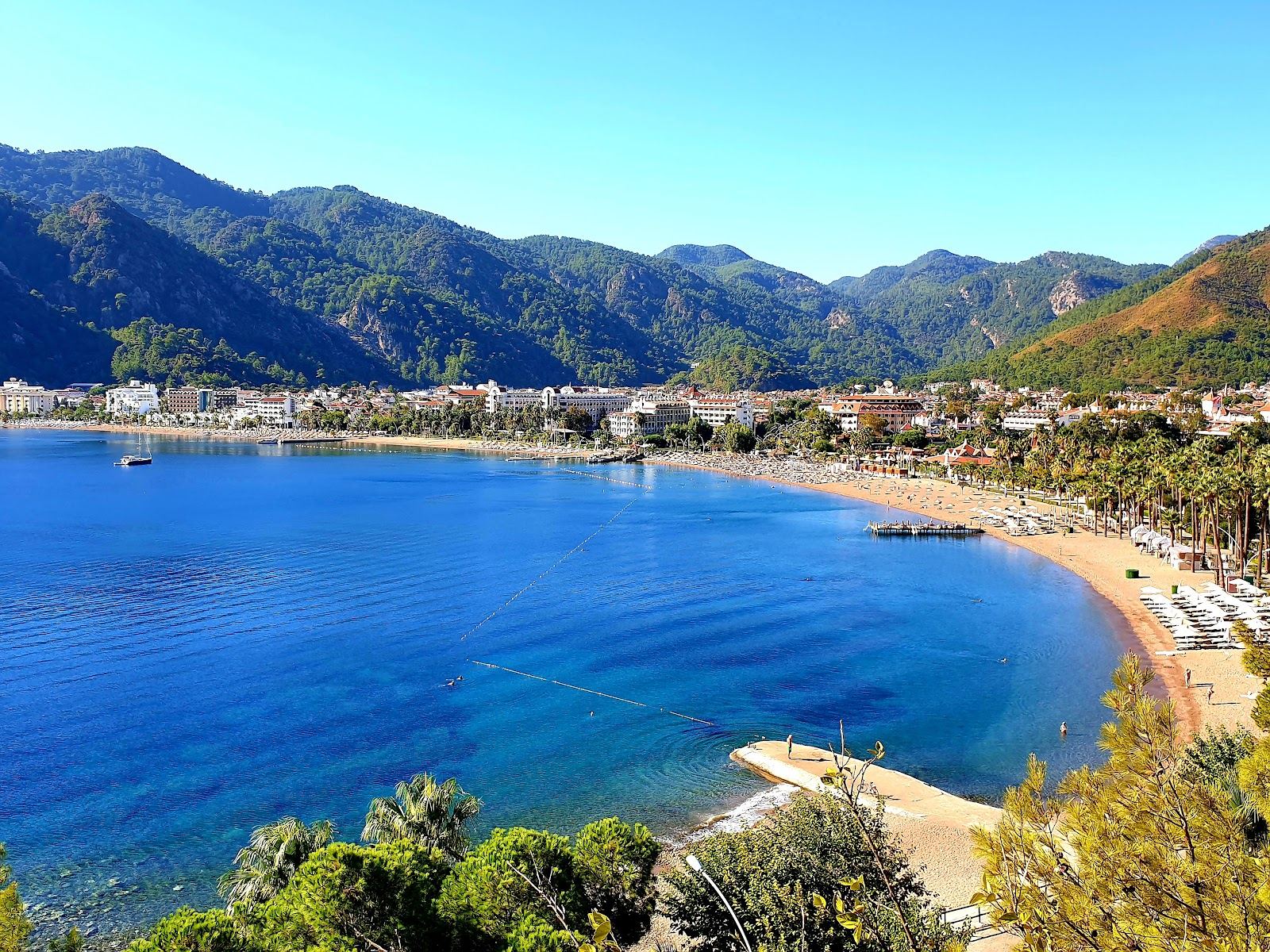 Icmeler beach southwest of Marmaris with clear water, golden sand and steep pine mountains behind in Turkey