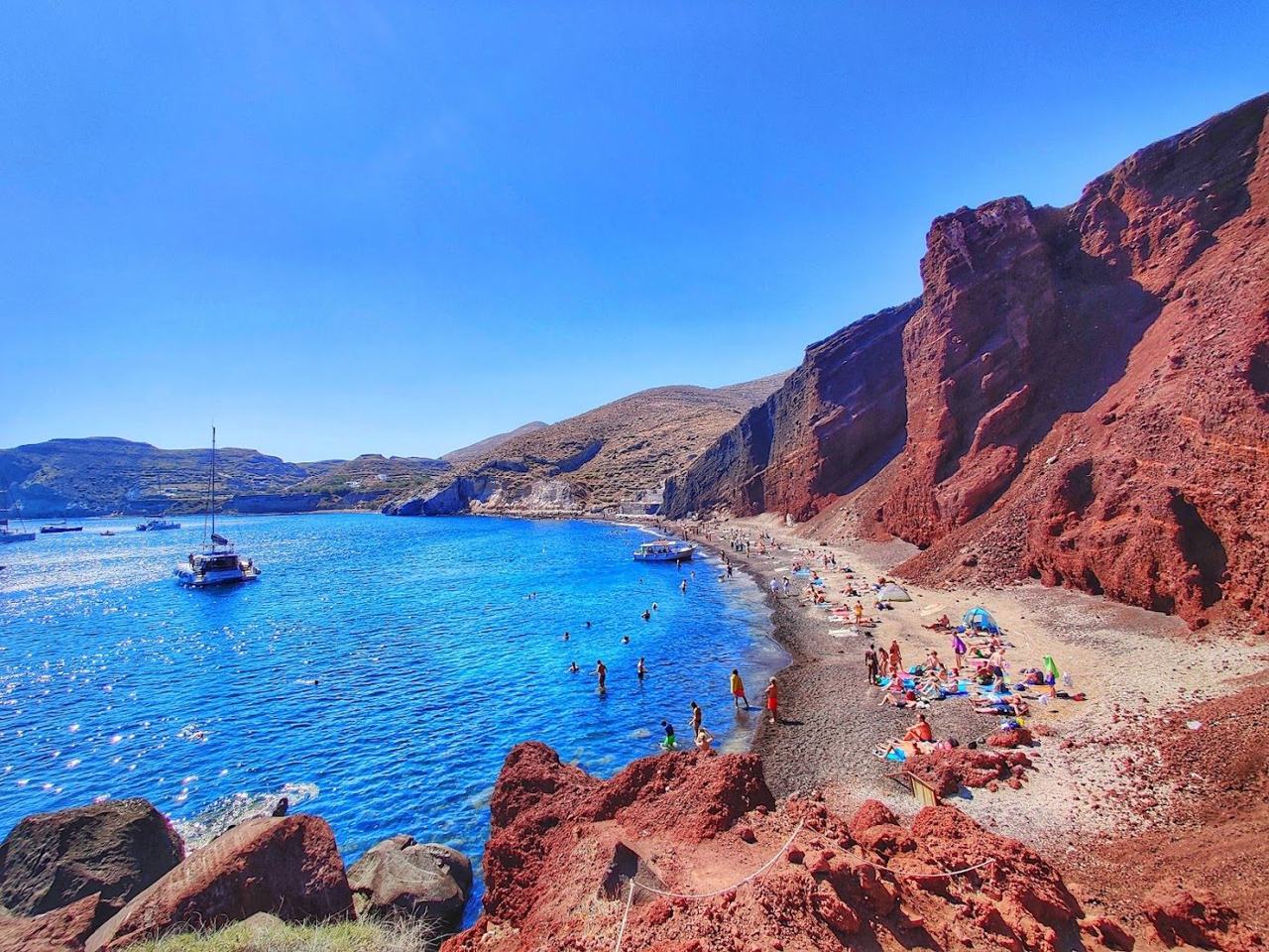 The red volcanic cliffs and dark sand of Red Beach on Santorini above clear water