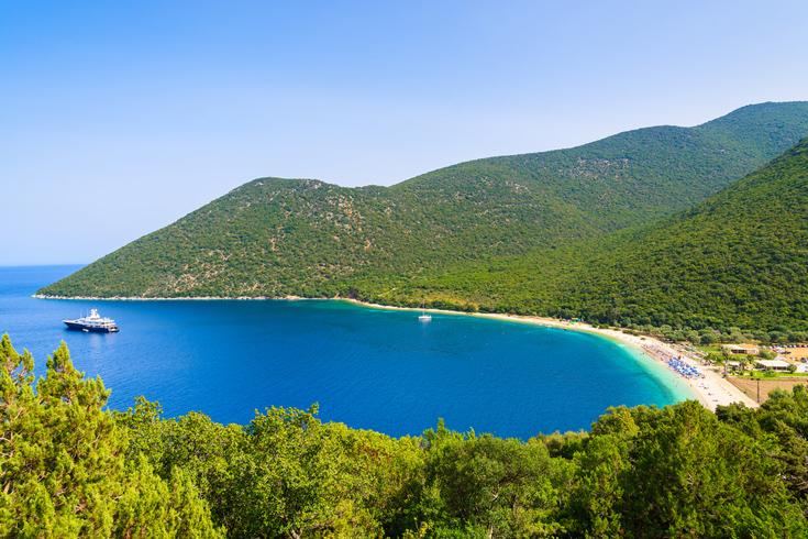 Green slopes meeting white pebbles along Antisamos bay near Sami