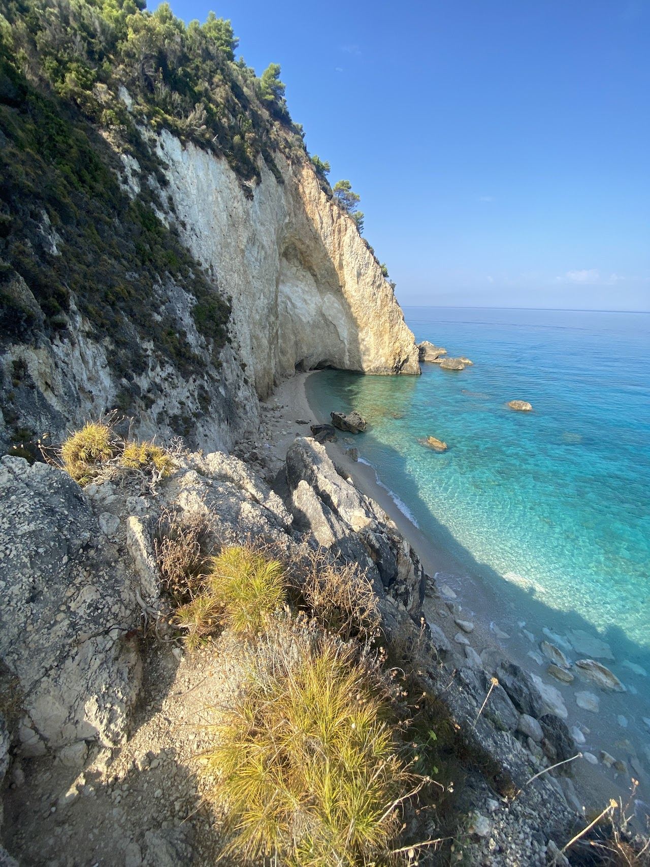 Golden evening light over a quiet cove of clear water and pale sand on the Lefkada coast