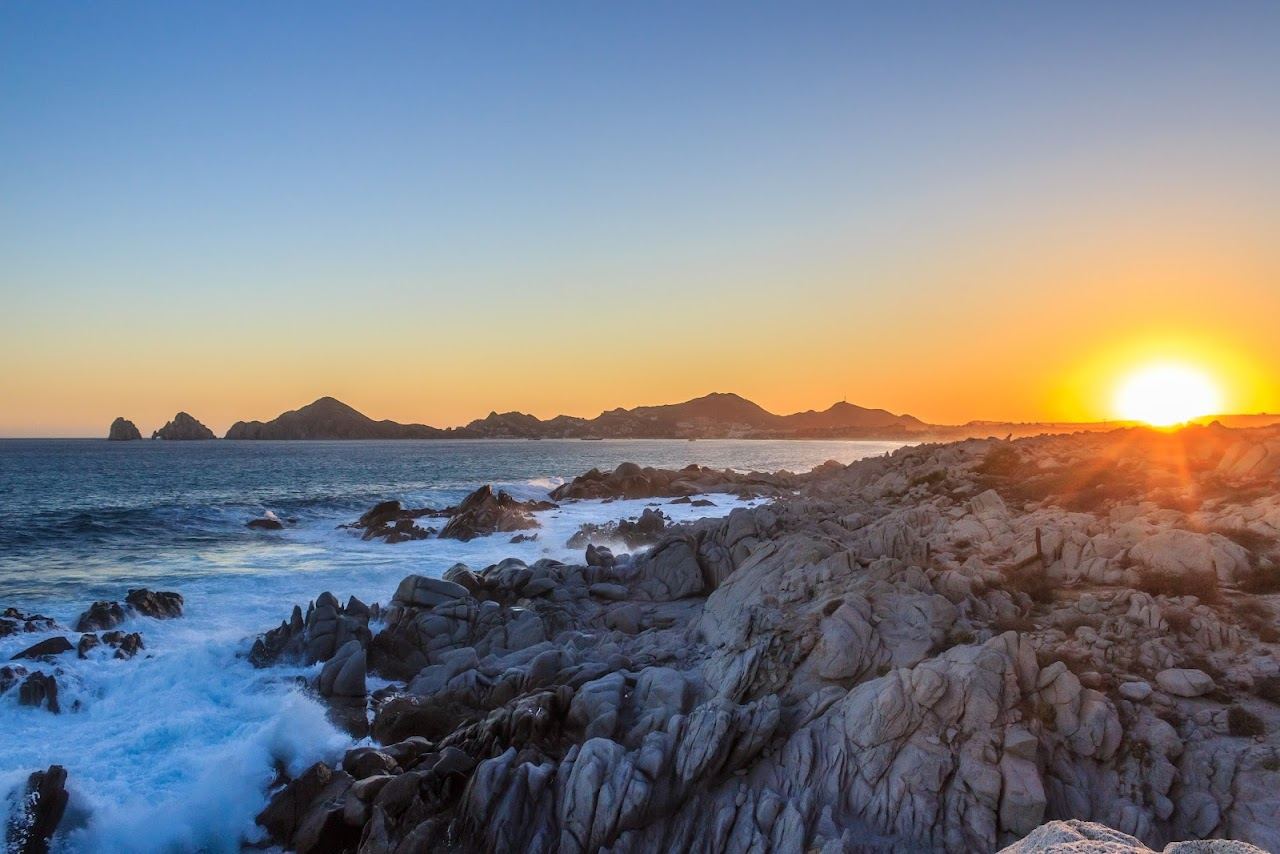 Waves breaking over the rocky point with the bay beyond at Monuments Beach in Cabo San Lucas