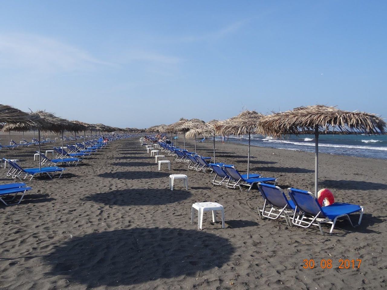The calm shallow water and soft dark sand of Monolithos Beach near the airport on Santorini