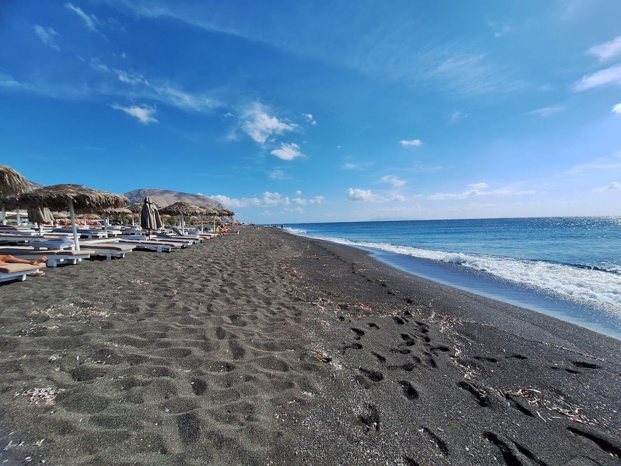 Day beds and umbrellas along the black sand beach club strip of Perivolos on Santorini