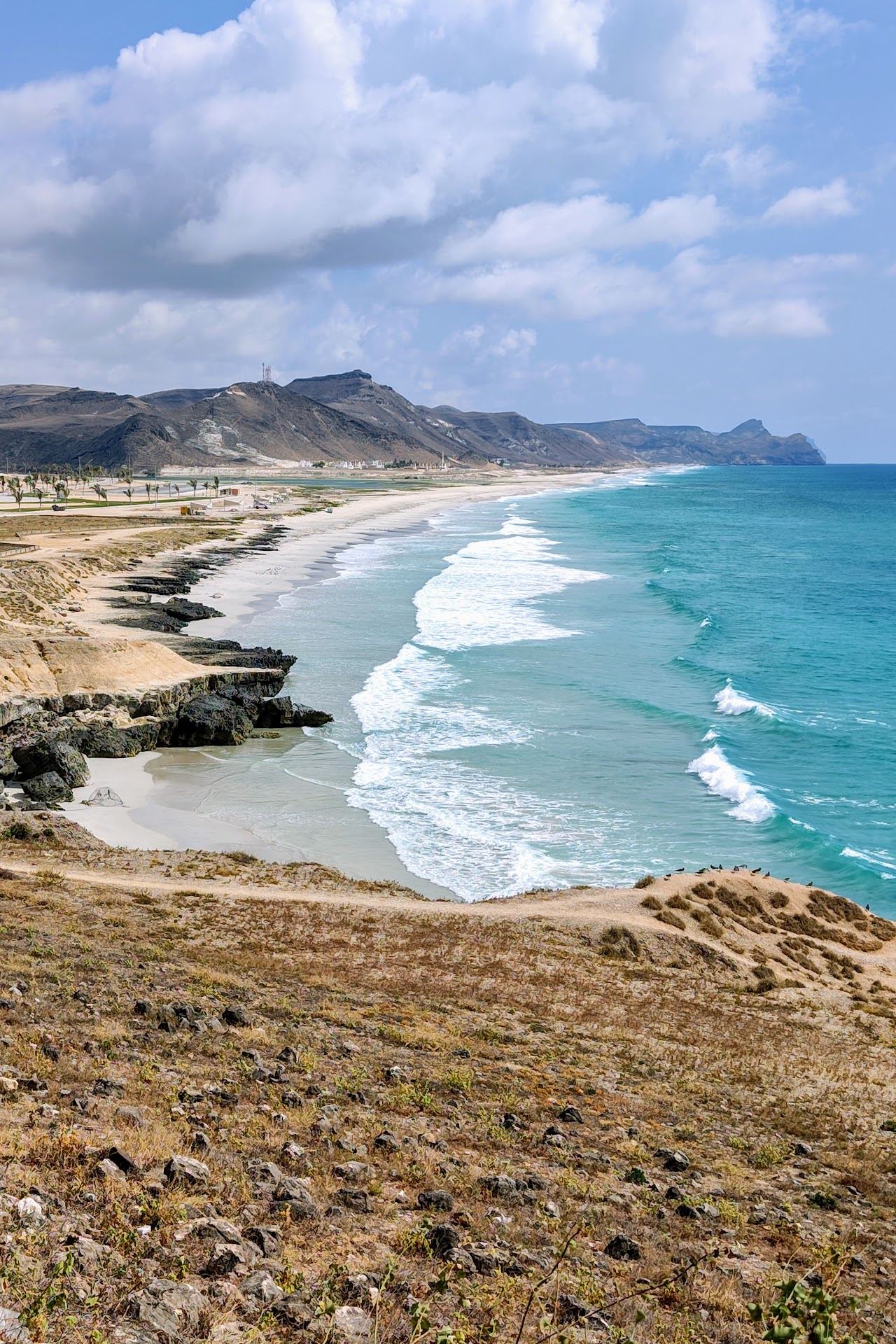 Pale sand and clear water below dramatic cliffs on the coast at Mughsail near Salalah in Oman